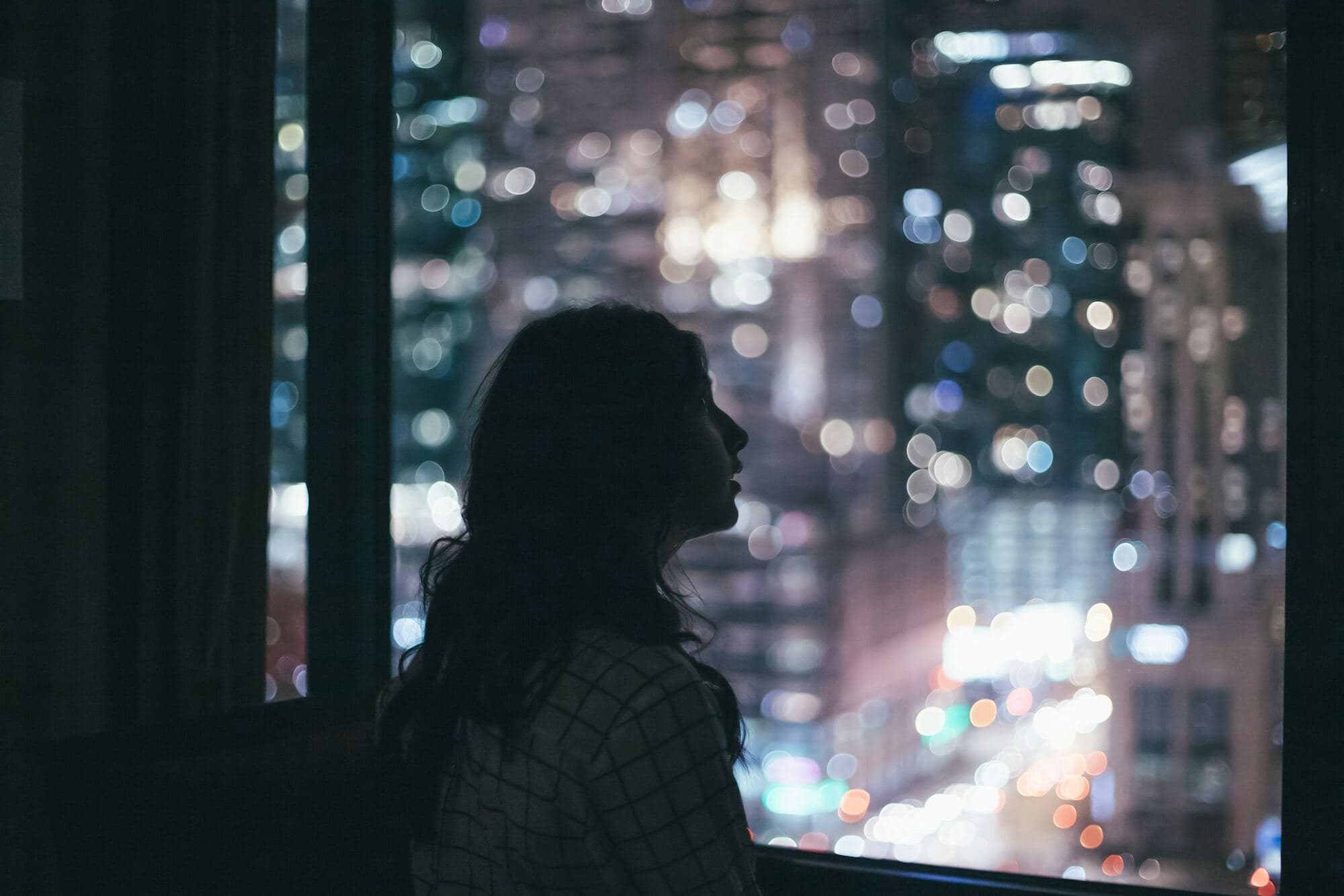 Una mujer mira por la ventana de noche, pensativa